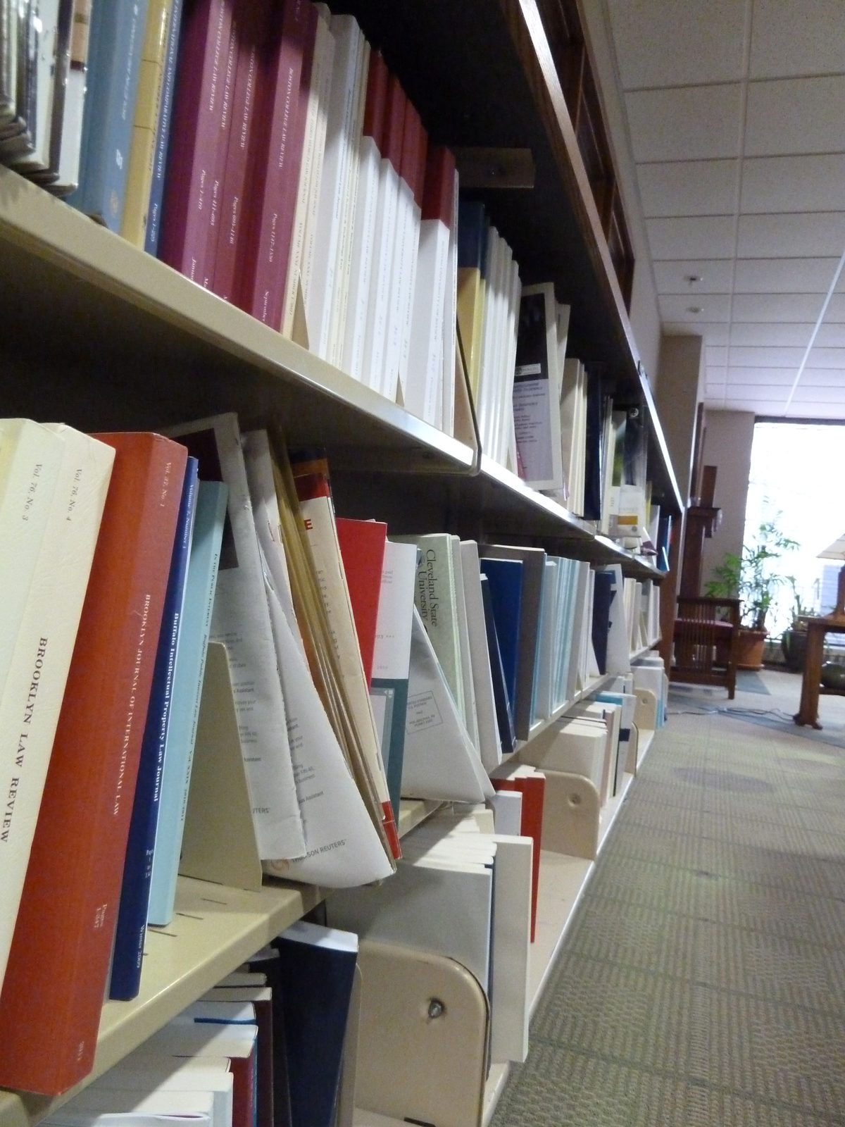 An angled view of a law-library shelf, with white, orange and blue volumes and visible gaps between books.